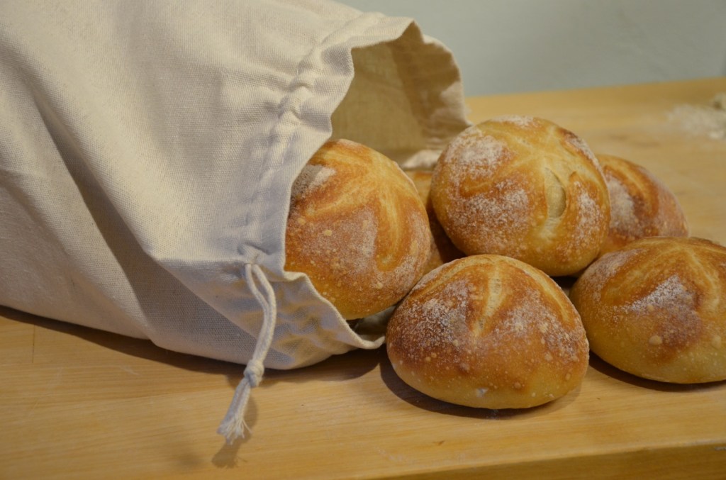 Hausgemachte knusprige Brötchen im Leinenbeutel auf Holztisch